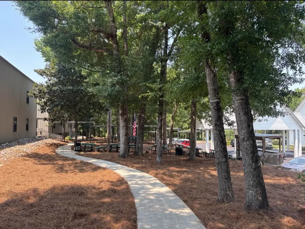 Straw beds Luckie's Pinestraw laid curving beside a shaded campus walkway and picnic tables — serving Perdido and the surrounding Gulf Coast